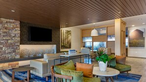 A modern hotel lobby with a stone accent wall, a flat-screen TV, a seating area with sofas and armchairs, a coffee table, and a potted plant. - Fairfield by Marriott Inn & Suites Sandusky (Sandusky)