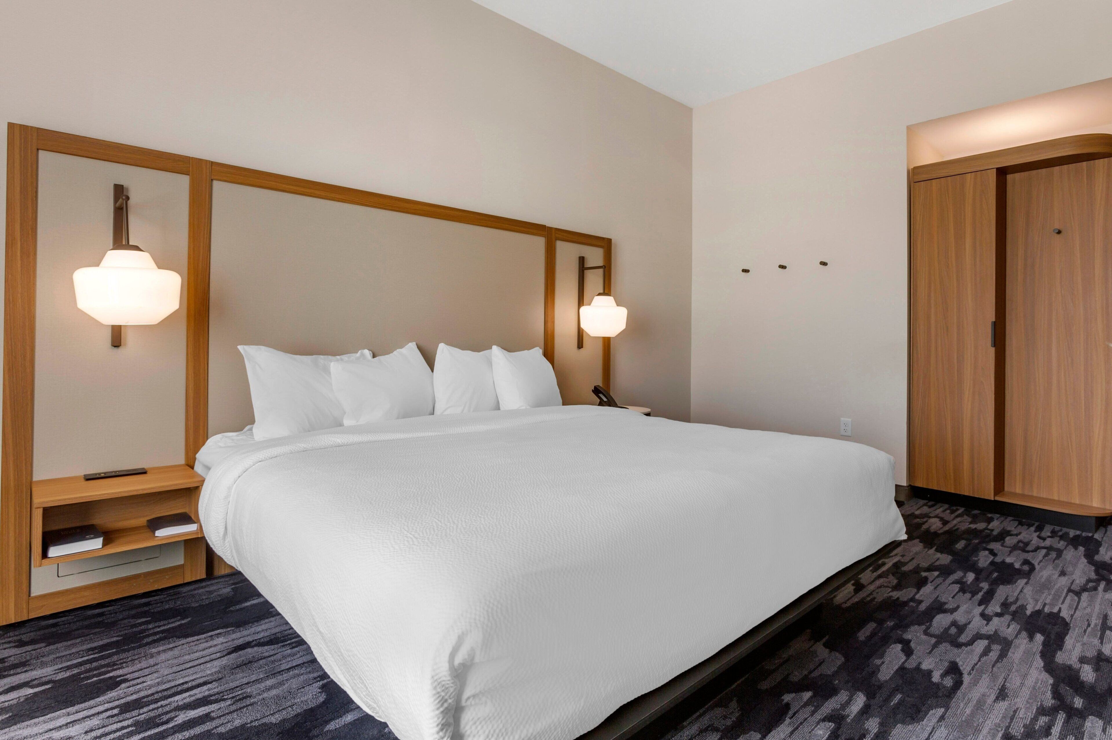 Ein Hotelzimmer mit einem großen Bett, einem Holzkopfschild, Nachttischen mit Lampen und einem Teppichboden.