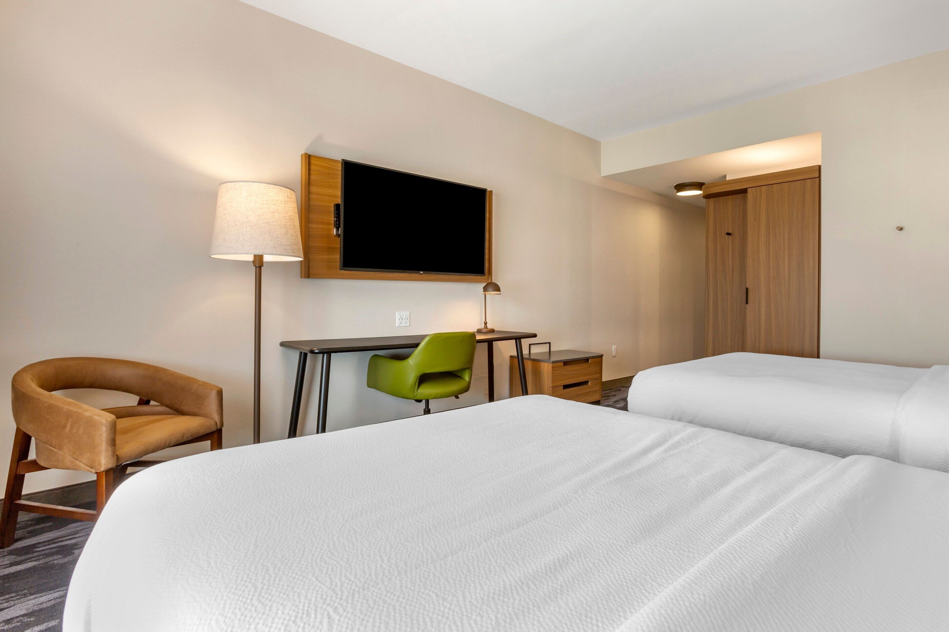A hotel room with two beds, a desk, a chair, a TV, and a wardrobe.