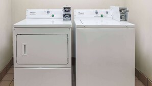 Two stacked Whirlpool front-loading washing machines in a corner with tiled flooring. - Super 8 by Wyndham Garland North Dallas Area (Garland)