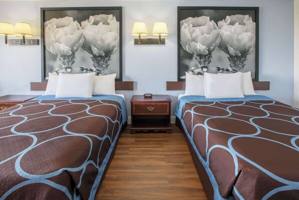 A hotel room with two beds, each with a brown and blue patterned bedspread, a nightstand with a lamp, and a wall-mounted light fixture. - Super 8 by Wyndham Garland North Dallas Area (Garland)
