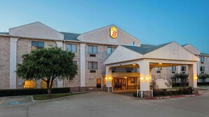 A hotel with a prominent '8' logo, a covered entrance, and a parking lot. - Super 8 by Wyndham Garland North Dallas Area (Garland)