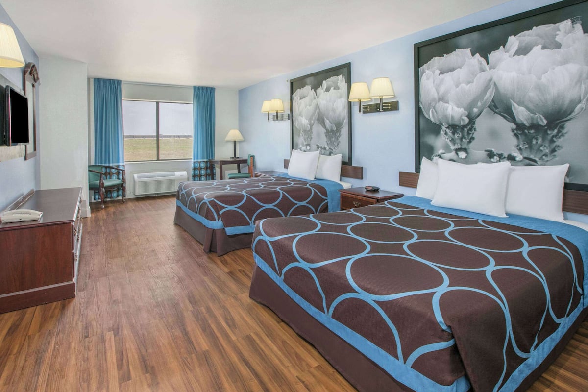 A hotel room with two beds, a desk, a chair, and a window with curtains.