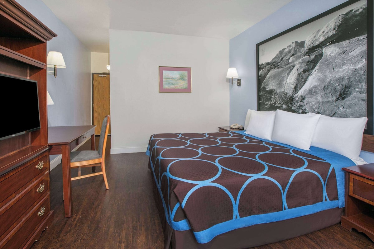A hotel room with a large bed, a desk with a chair, a television, and a painting on the wall.