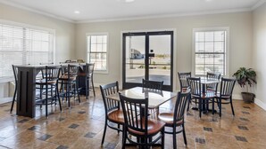 A spacious dining area with a large round table and multiple chairs, a kitchen area with a bar counter, and large windows providing natural light.