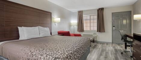 A hotel room with a large bed, a desk, a chair, and a wardrobe.