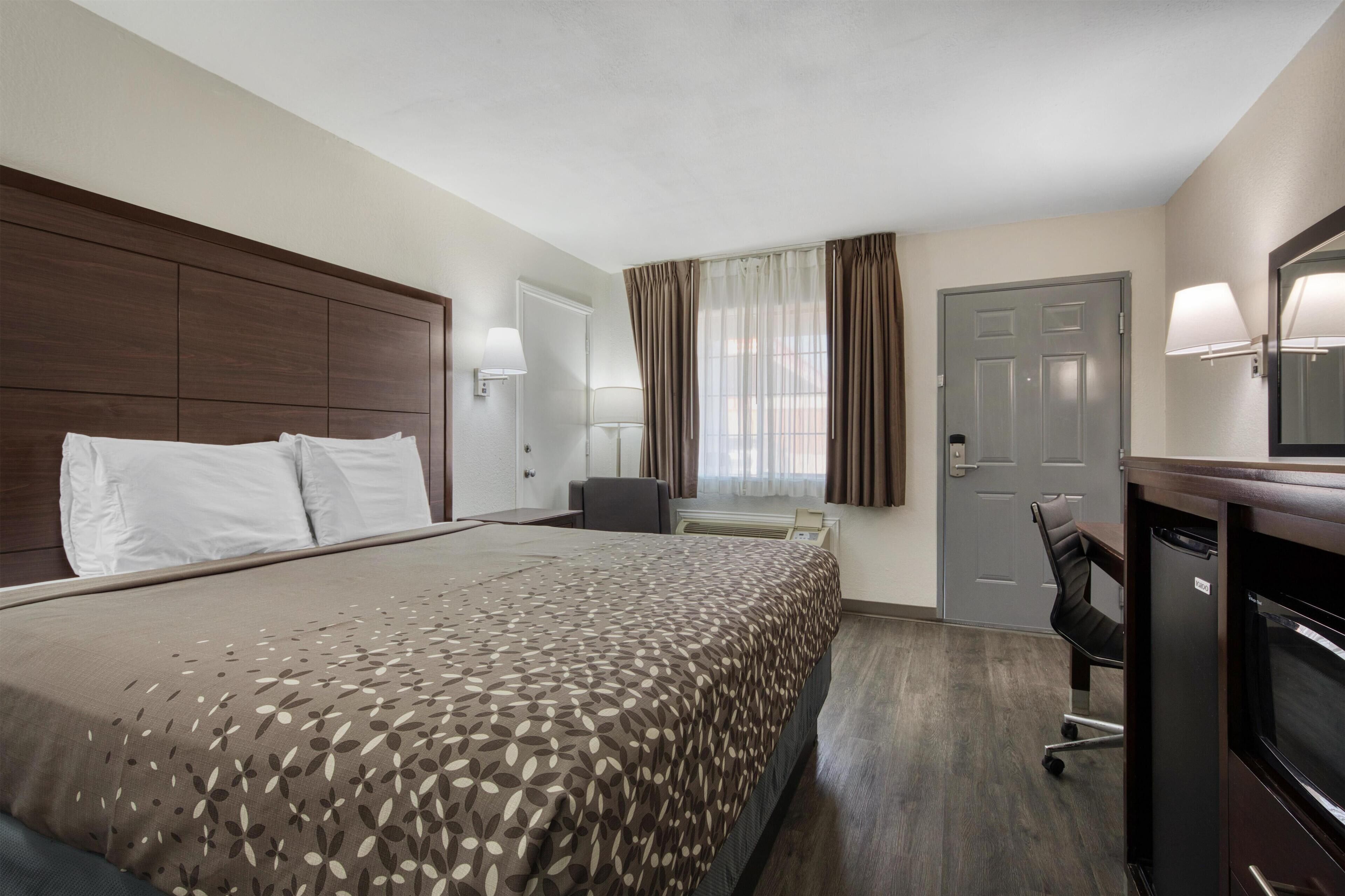 Ein Hotelzimmer mit einem großen Bett, einem Schreibtisch, einem Stuhl, einem Kühlschrank und einer Tür.