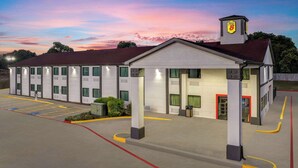 A motel with a row of rooms, a parking lot, and a small tower with a sign. - Super 8 by Wyndham Waxahachie TX (Waxahachie)