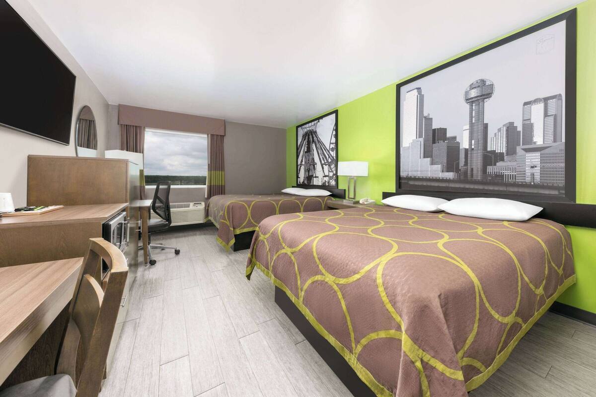 A hotel room with two beds, a desk, a chair, a TV, and a large window.