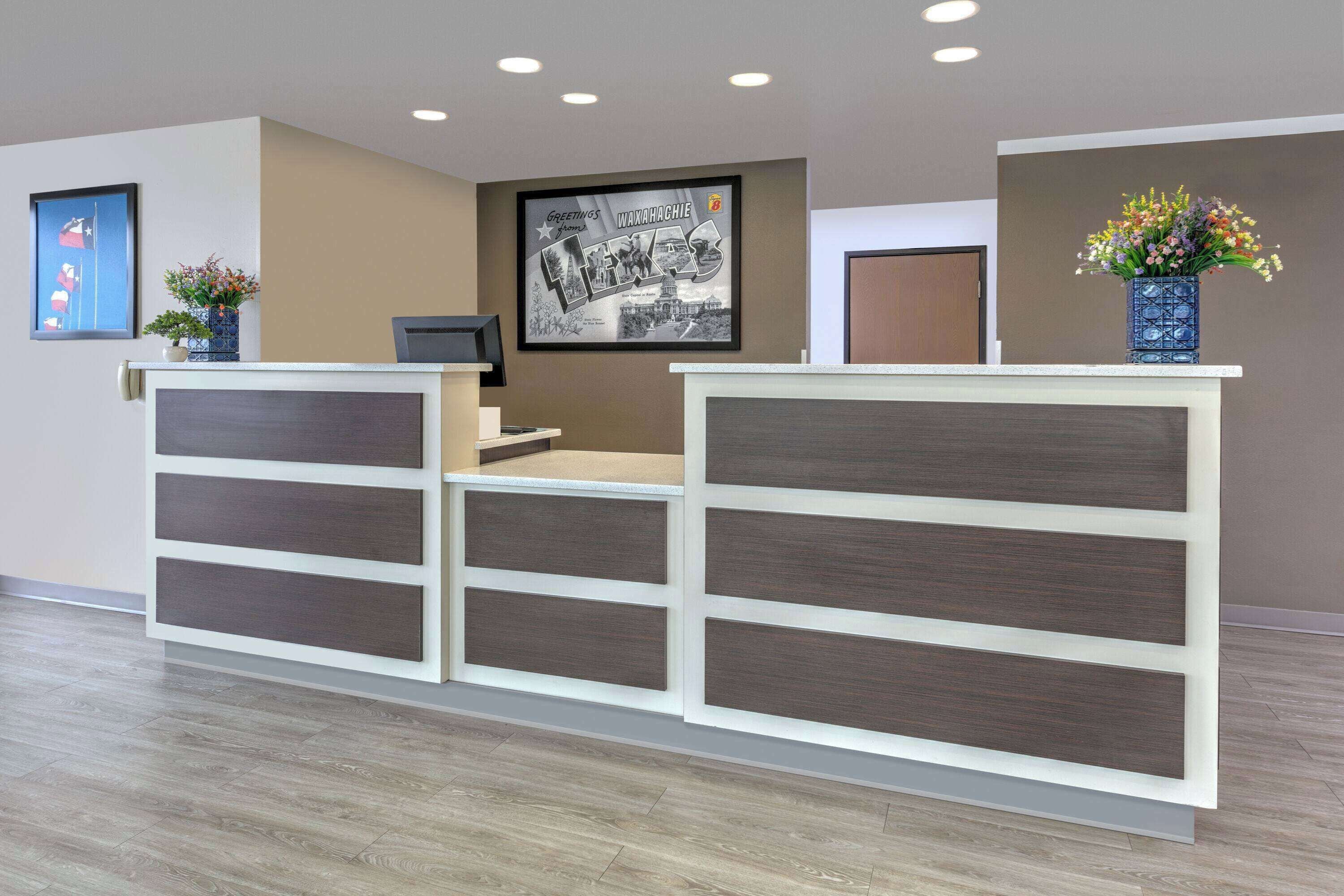 A reception desk with a framed welcome sign, a small plant, and a vase of flowers.