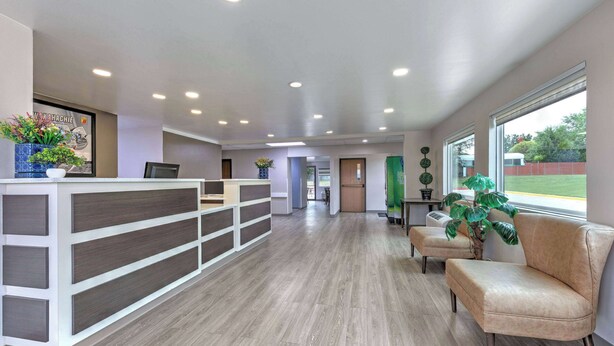 A reception area with a wooden reception desk, a beige sofa, and potted plants. - Super 8 by Wyndham Waxahachie TX (Waxahachie)
