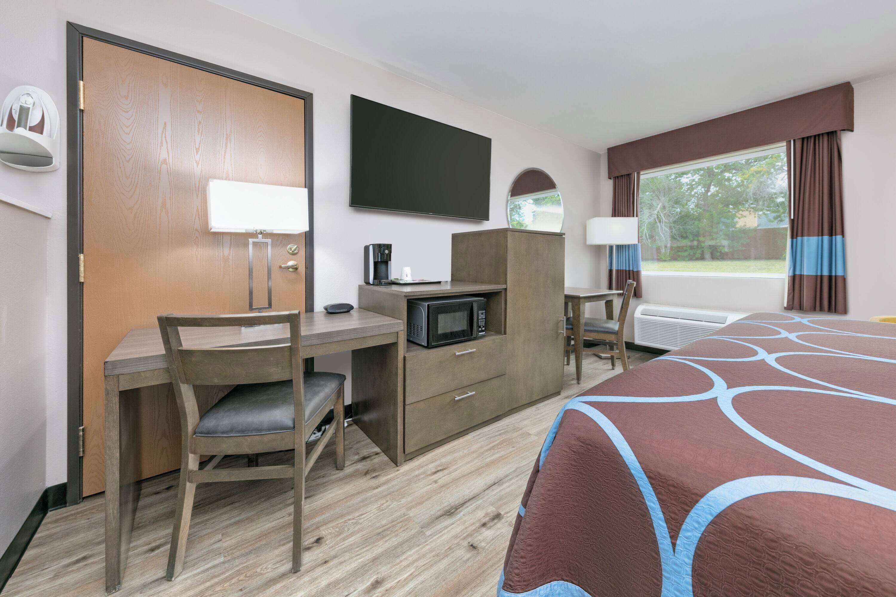 A hotel room with a bed, a desk with a chair, a television, a microwave, and a window with curtains.