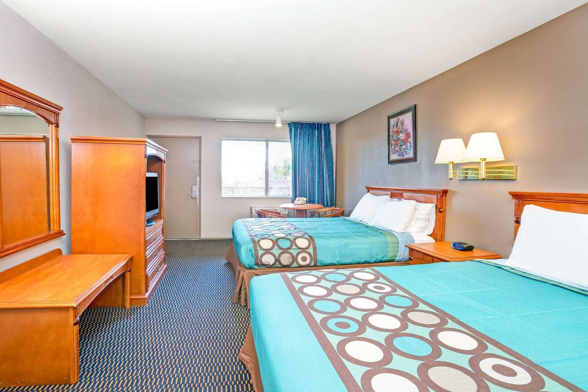 A hotel room with two beds, a desk, a dresser, a TV, and a window with curtains.