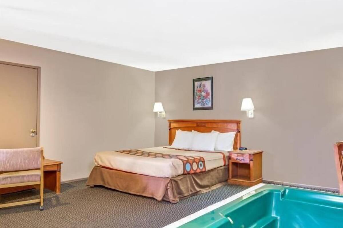A hotel room with a bed, bedside tables, a desk, a chair, a small pool, and a door.