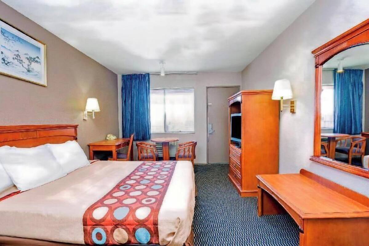 A hotel room with a bed, a desk, a chair, a dresser, a mirror, a lamp, and a window.