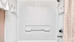 A bathroom with white tiled walls, a white bathtub, a towel rack, and a shower curtain.