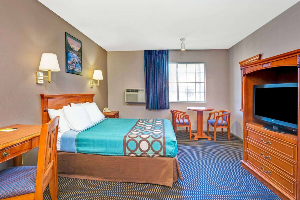 A hotel room with a bed, a desk, a chair, a television, and a window with curtains.