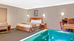 A hotel room with a bed, a desk, a chair, a small table, a pool table, and a painting on the wall.
