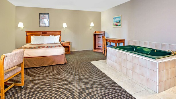A hotel room with a bed, a desk, a chair, a small cabinet, a bathtub, and two wall-mounted lamps.