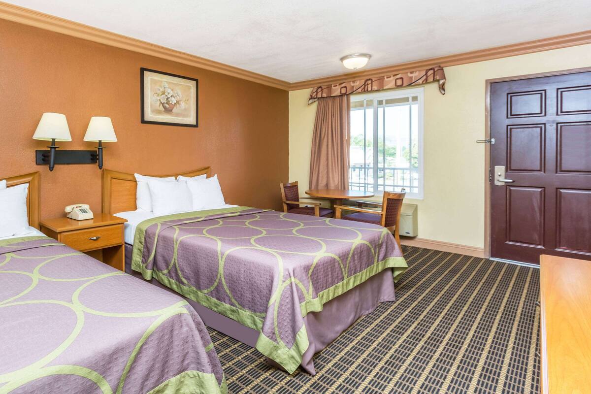 A hotel room with two beds, a desk, a chair, a phone, and a door.