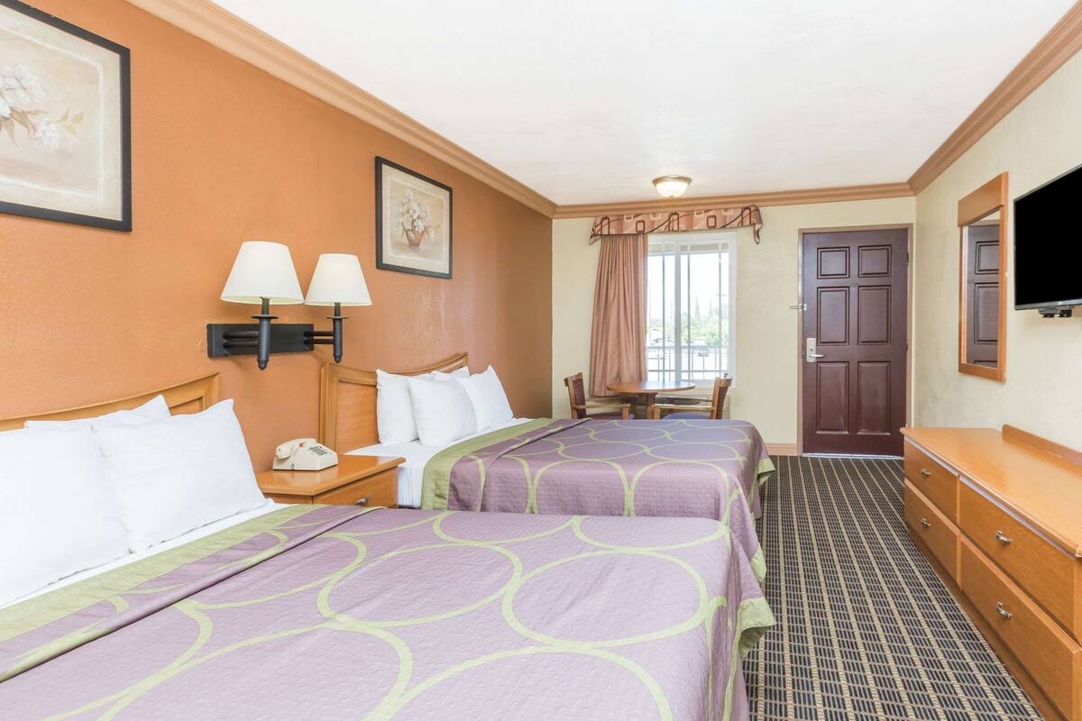 A hotel room with two beds, a desk, a chair, a TV, and a door.