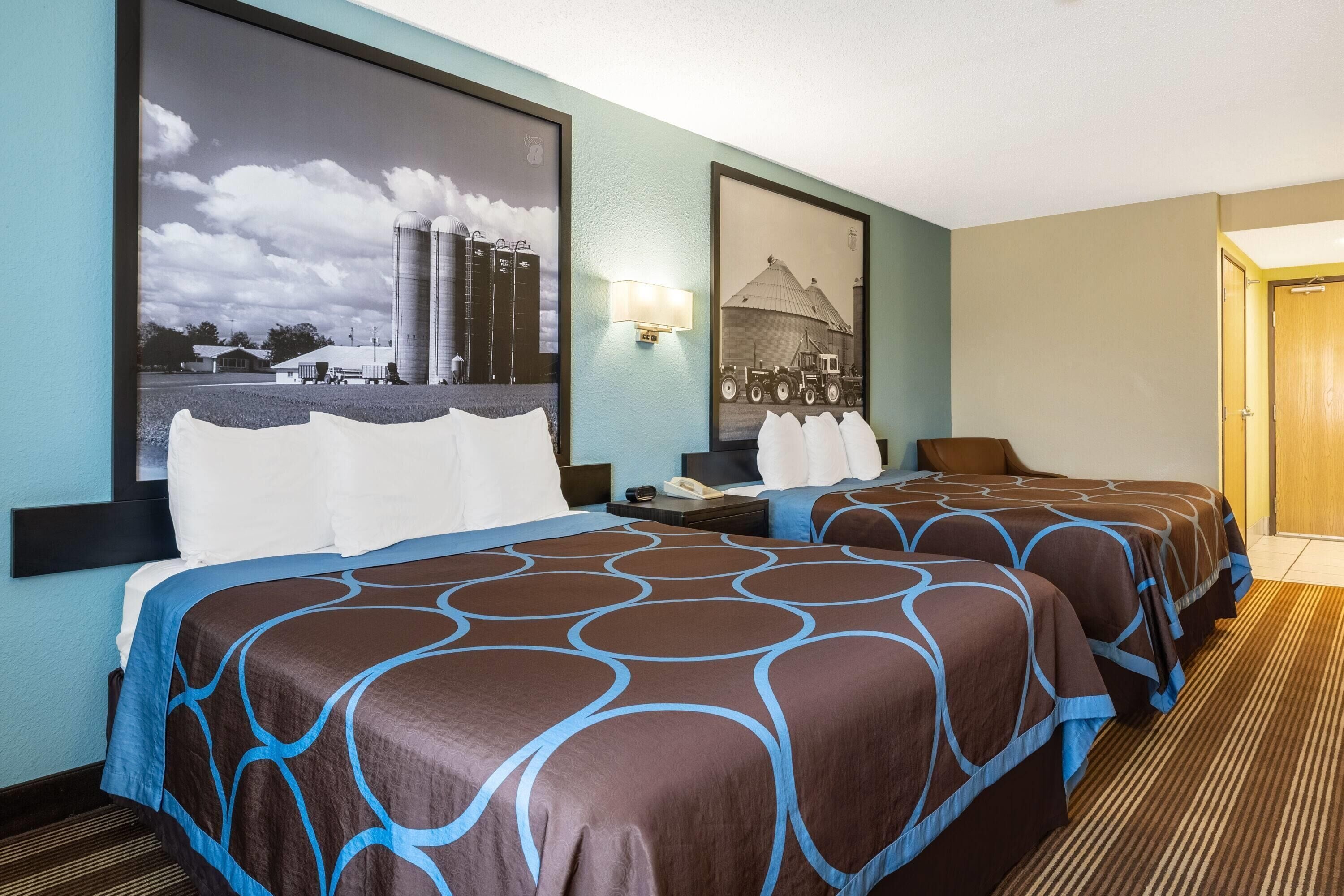 A hotel room with two beds, a large window, and a framed picture on the wall.