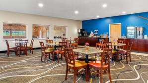 Une salle à manger d’hôtel avec de nombreuses tables et chaises, un espace cuisine et une vue sur l’extérieur grâce à de grandes fenêtres.
