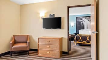 A hotel room with a brown leather chair, a wooden chest of drawers, a flat-screen TV, and a bed with a patterned bedspread.