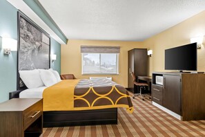 Habitación de hotel con cama, escritorio, televisor y ventana con vista a un estacionamiento.