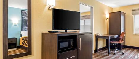 Habitación de hotel con una televisión de pantalla plana sobre un mueble de madera, un escritorio con una silla y un espejo grande en la pared.