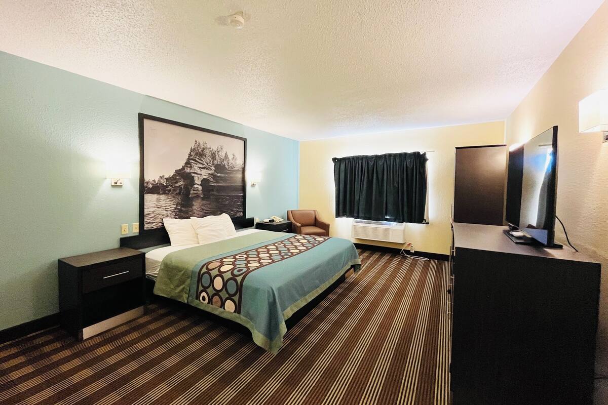 Ein Hotelzimmer mit Bett, Schreibtisch, Stuhl, Fernseher und einem fensterbepflanzten Fenster.