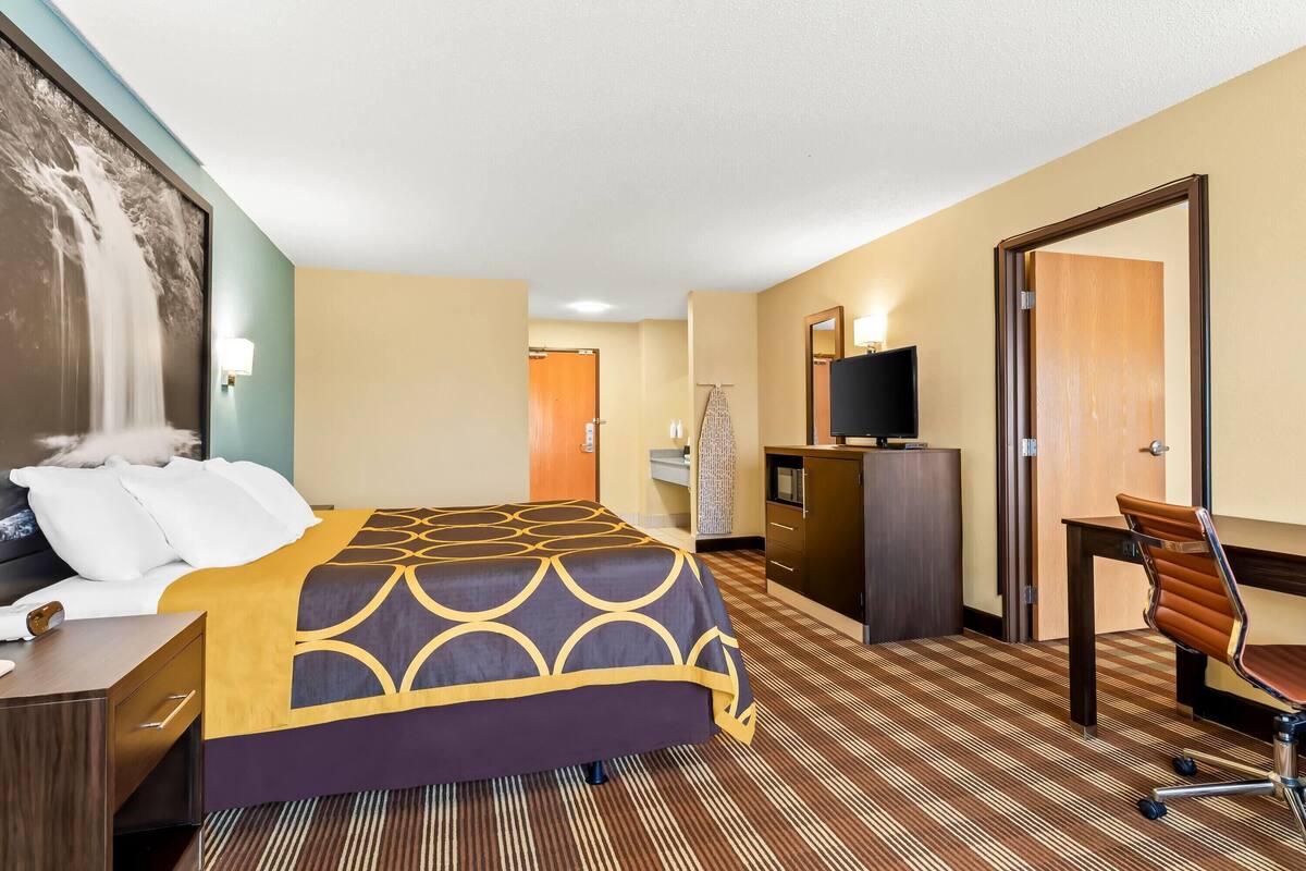 Ein Hotelzimmer mit Bett, Schreibtisch, Sessel, Fernseher und Kleiderschrank.