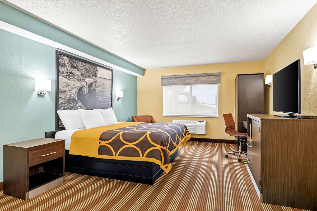 Ein Hotelzimmer mit Bett, Schreibtisch, Fernseher und einem Fenster mit Jalousien.