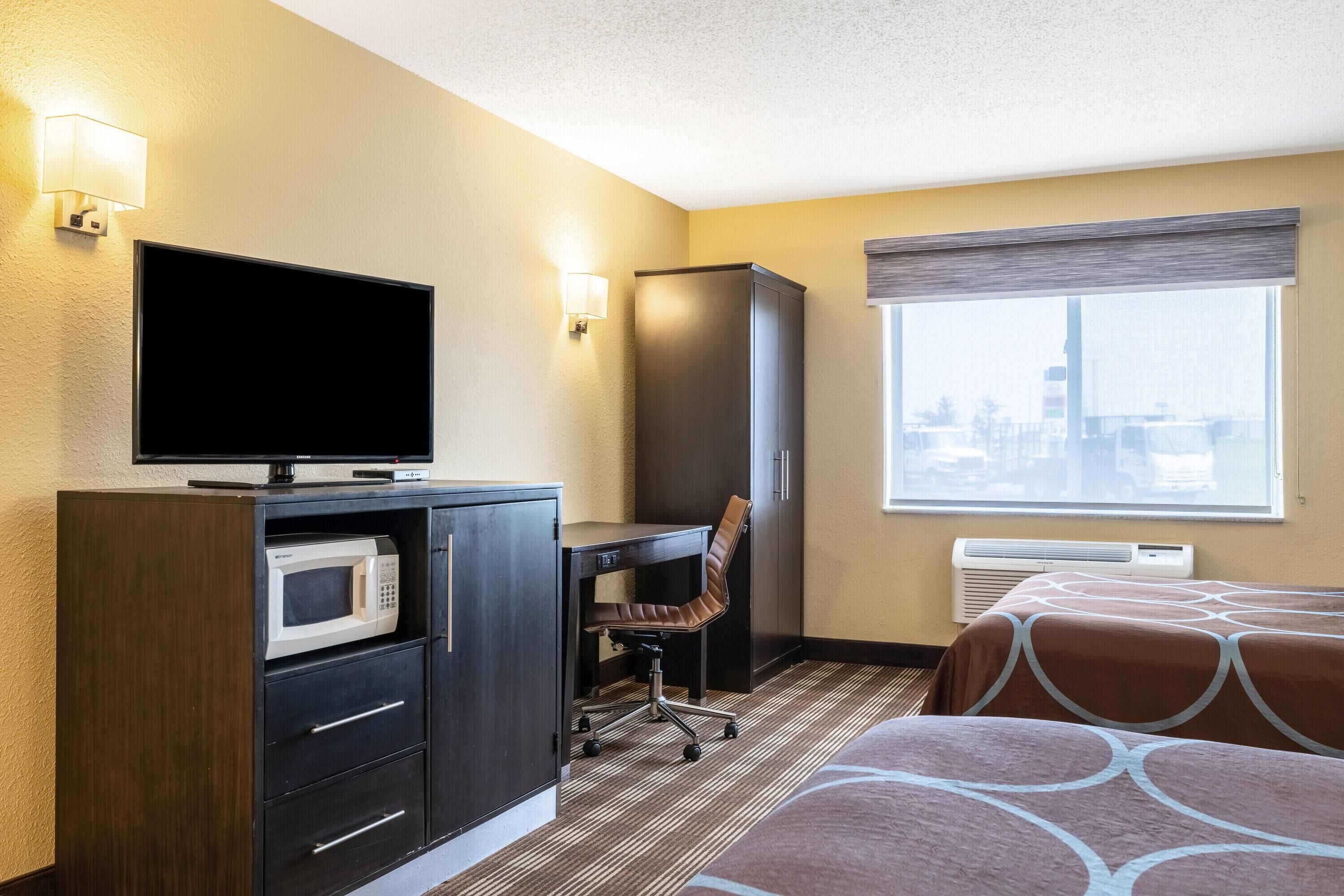 A hotel room with a flat-screen TV, a microwave, a desk with a chair, and two beds.