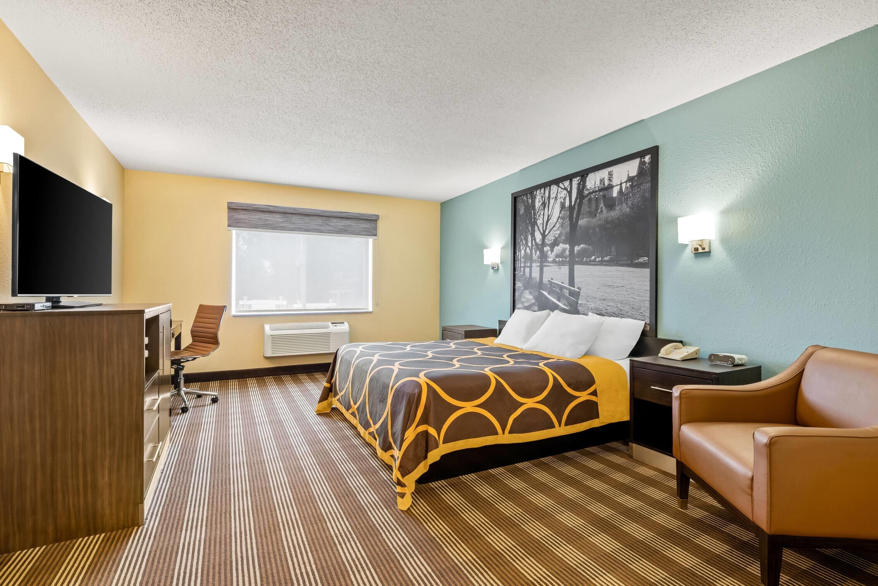 A hotel room with a bed, a desk, a chair, a TV, and a window.