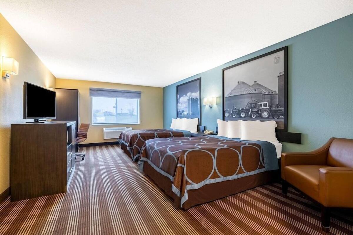 Ein Hotelzimmer mit zwei Betten, einem Schreibtisch mit Fernseher, einem Fenster und einem gerahmten Bild an der Wand.