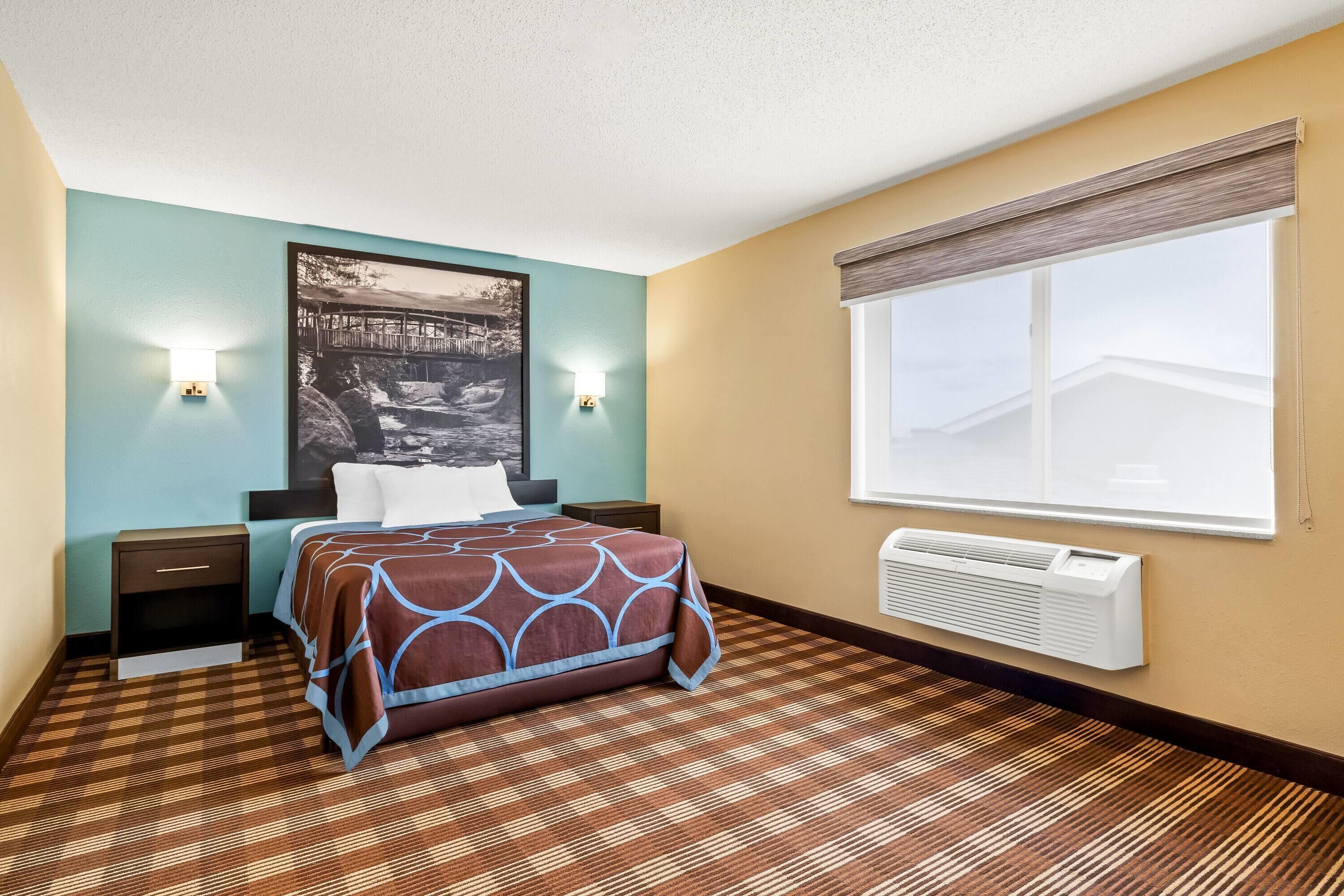Ein Hotelzimmer mit Bett, Nachttischen, einer Wand-Klimaanlage und einem großen Fenster.