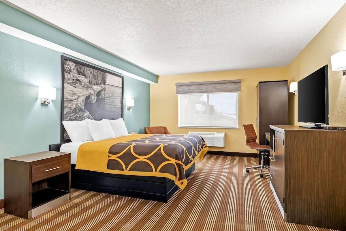 Ein Hotelzimmer mit Bett, Schreibtisch, Fernseher und Fenster.