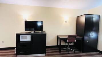 Een hotelkamer met een bureau, een stoel, een televisie, een magnetron en een kledingkast.