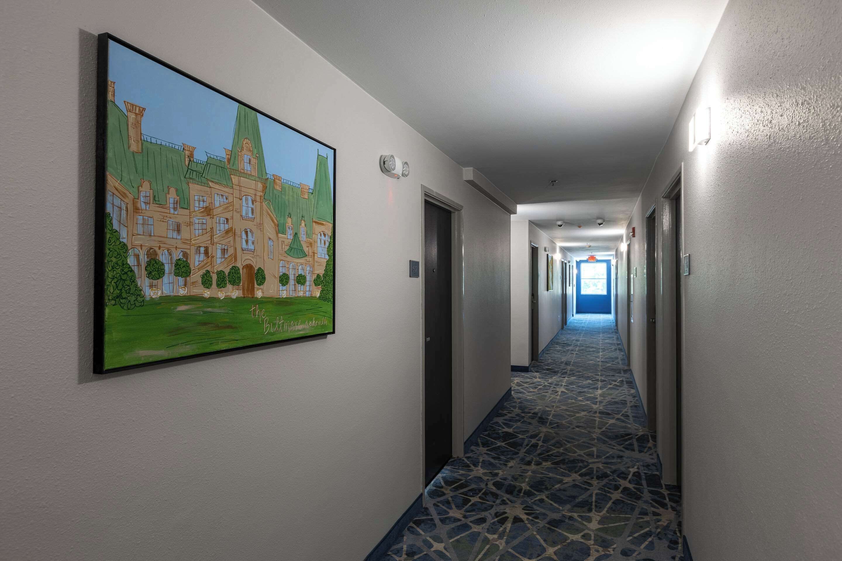 A hotel hallway with a large painting of a building, a tiled floor, and doors leading to rooms.