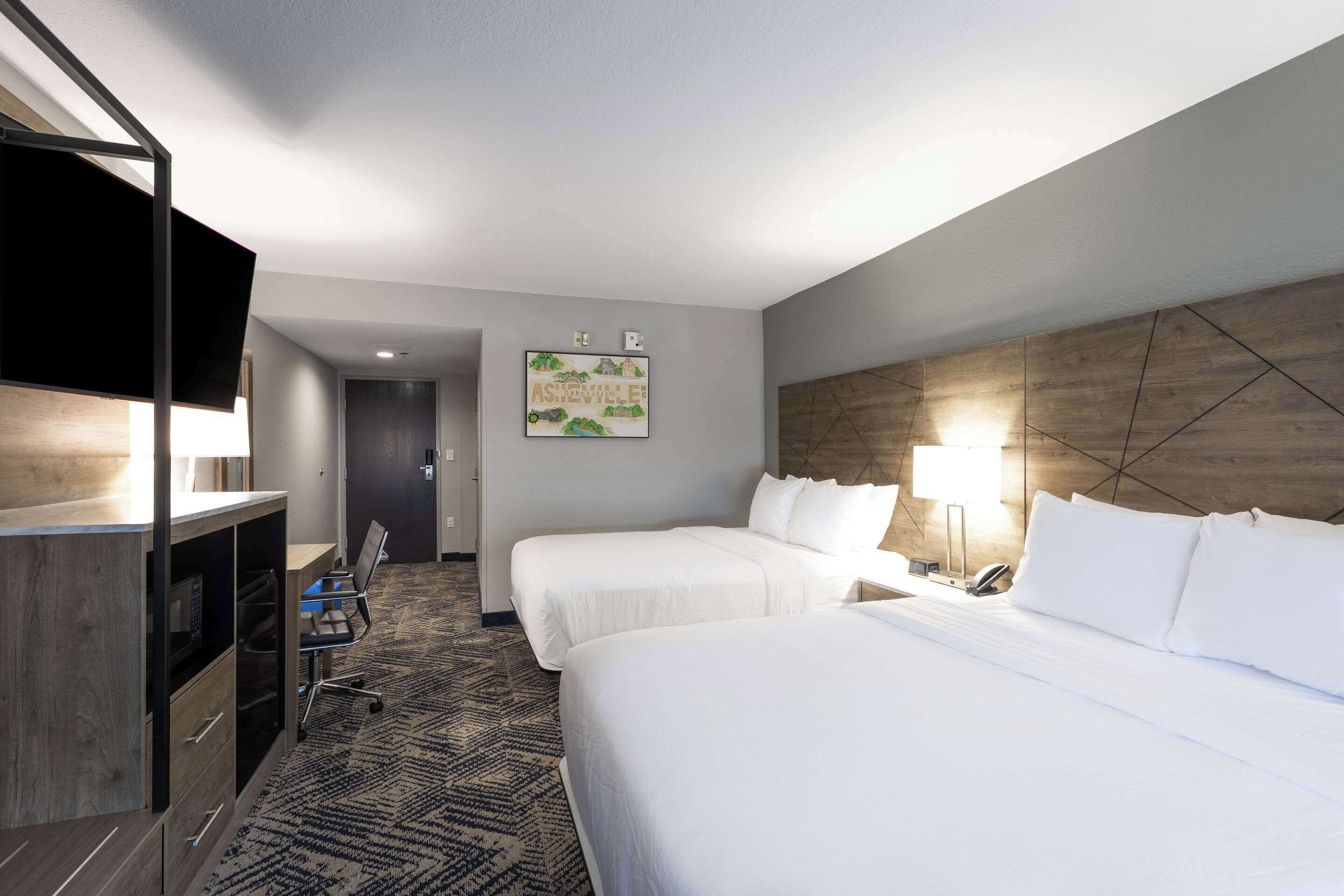 Une chambre d’hôtel avec deux lits, un bureau, une chaise et un téléviseur.