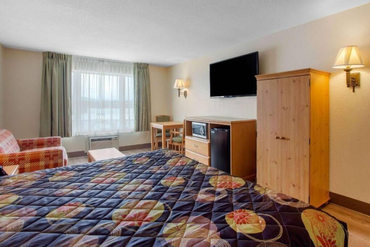 Quarto de hotel com cama, escrivaninha, televisão e guarda-roupa.