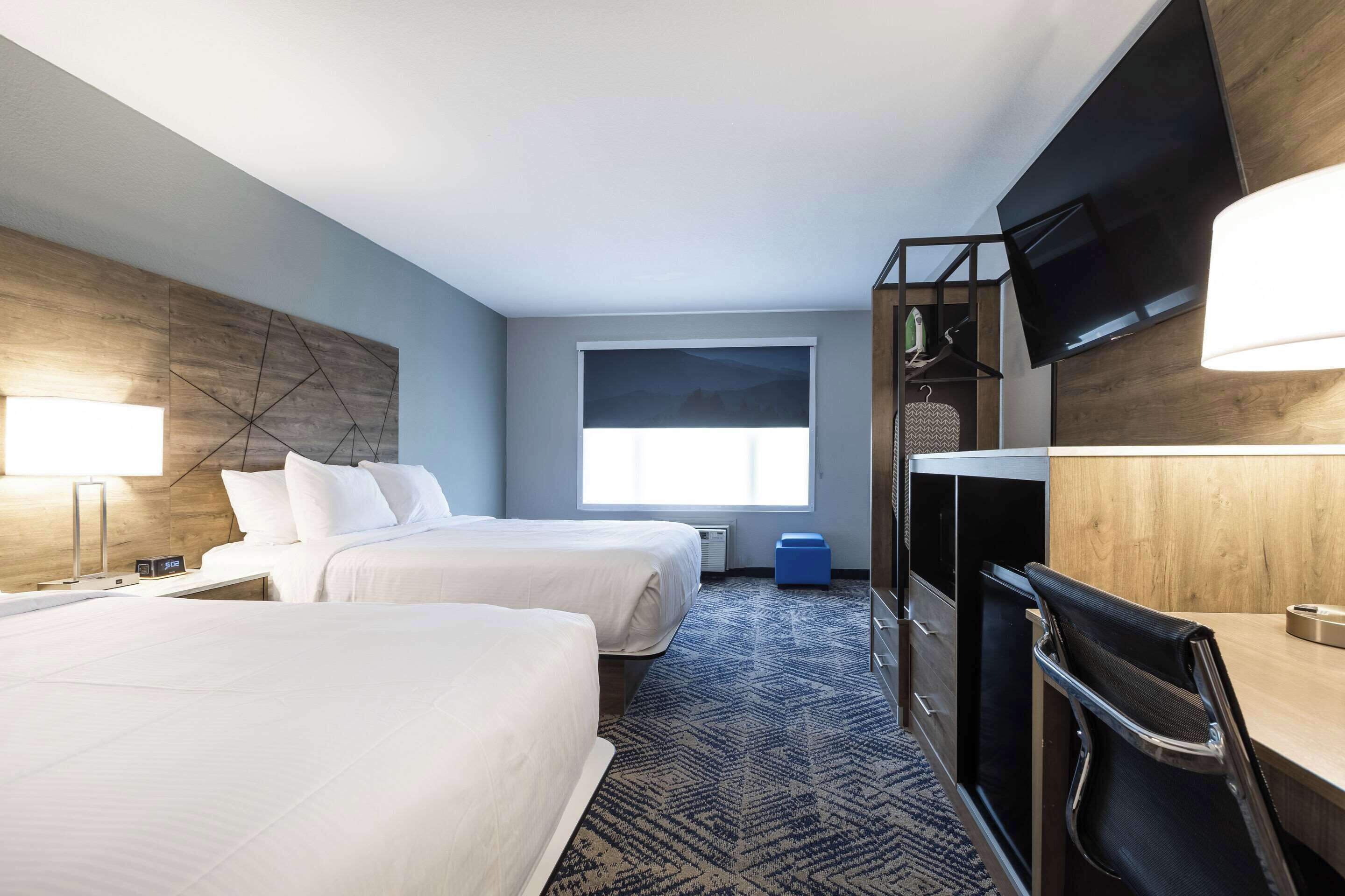 A hotel room with two beds, a desk, a chair, a TV, and a window with a view.