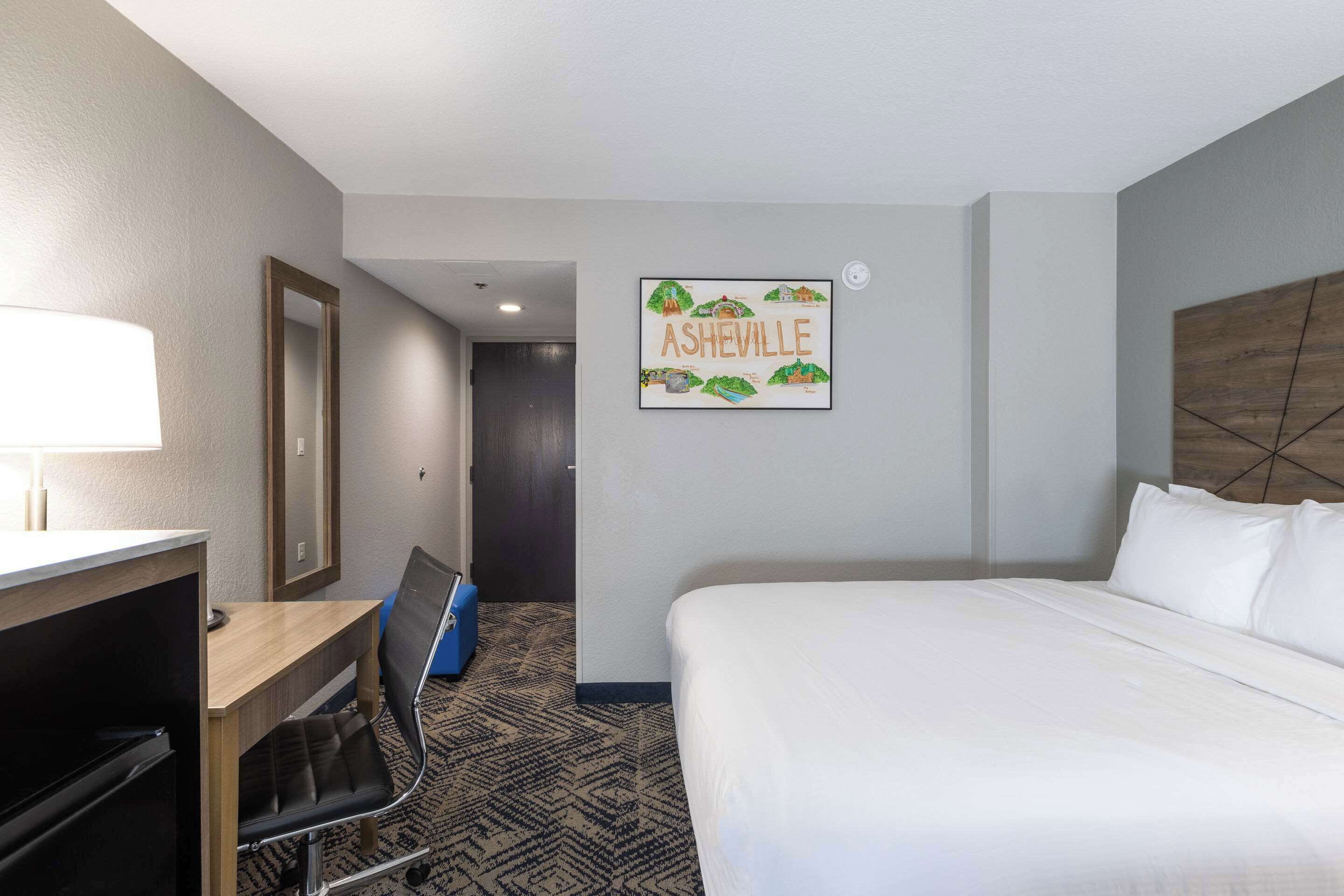 Ein Hotelzimmer mit Bett, Schreibtisch, Stuhl und einem an der Wand hängenden Bild von Asheville.