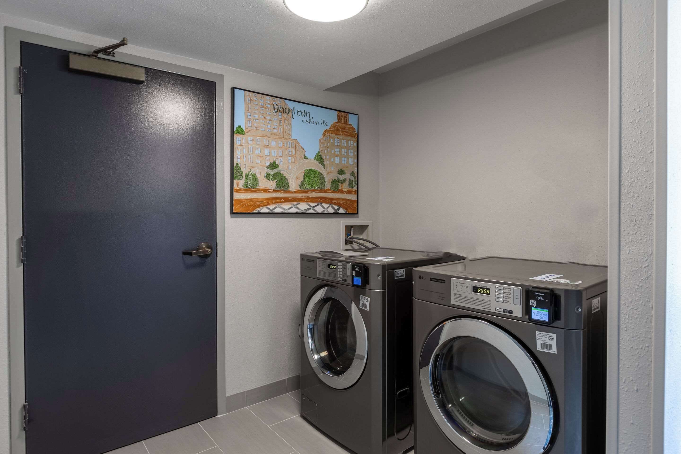 A laundry room with two front-loading washing machines, a dark door, and a wall-mounted poster of a cityscape.