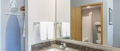 A bathroom with a granite countertop sink, a mirror, and a shower visible through an open door.