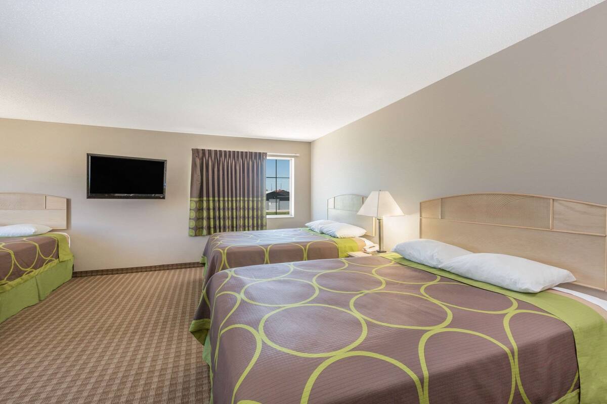 A hotel room with two beds, a flat-screen TV, a window with curtains, and a lamp.