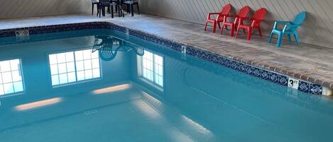 Una piscina interior con borde de azulejos, algunas sillas y un banco.