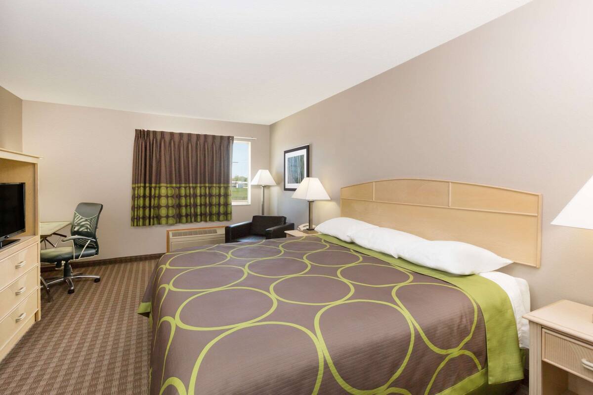 A hotel room with a large bed, a desk with a chair, a television, and a window with curtains.