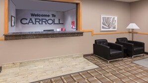 A reception area with a 'Welcome to CARROLL' sign, a reception desk, black leather chairs, a patterned carpet, and a framed artwork on the wall. - Super 8 by Wyndham Carroll/East (Carroll)